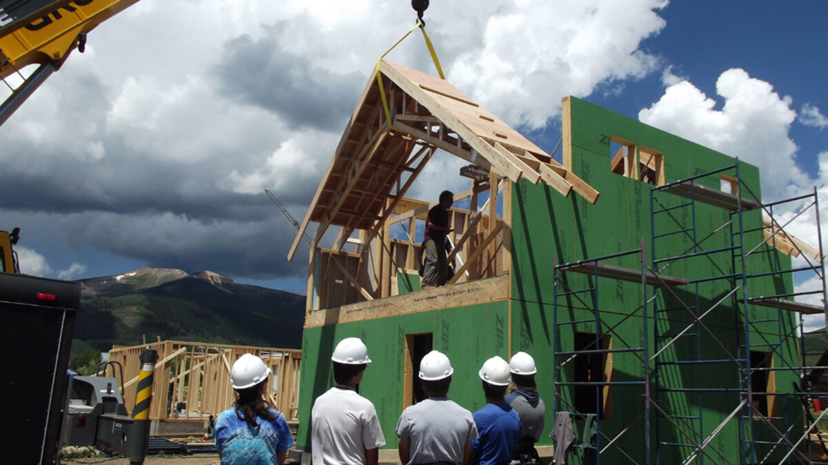 Students in hard hats watching roof framing being lifted into place